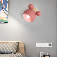 A  Mickey Mouse style Pink wall sconce with E27 sockets attached to a wall over  a bed.