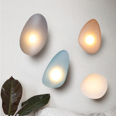 Golden Atelier LED wall lights in a modern glass pebble design, mounted on a wall and casting a warm glow. Blue Smoky Grey Smoky Amber White