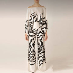 A female model wearing a satin off-shoulder top with long pants, featuring a striped pattern in shades of , white, and black.