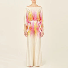 A female model wearing a satin off-shoulder top with long pants, featuring a striped pattern in shades of pink, orange.