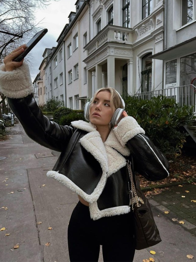 A person standing on a sidewalk wearing a black and white double sided thick lapel fleece jacket with front button closure and side pockets.