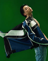 Model wearing a blue and black patchwork jacket on a green background.