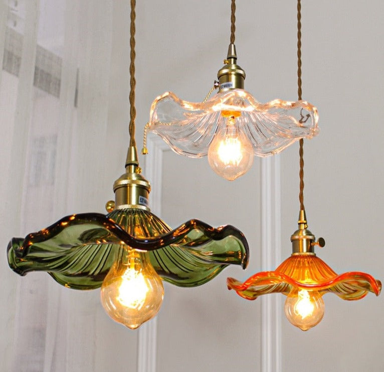 Three pendant LED lights with colourful glass shades in blue, champagne,  red, ink green, as flowers with polished copper finishes, and hanging from the ceiling.