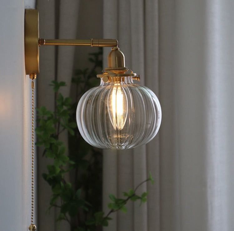 A modern glass globe wall light with a pull chain switch and brass finish.