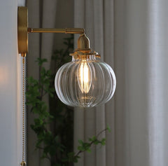 A modern glass globe wall light with a pull chain switch and brass finish.