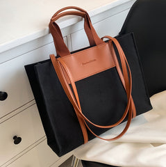 A canvas crossbody tote bag with brown leather handles and a tan patch on the front, displayed against a neutral background.