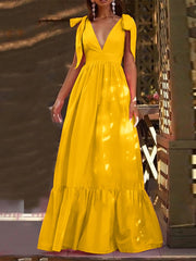 A model wearing a yellow deep V neck bow tie maxi dress with cap sleeves and a pleated skirt.
